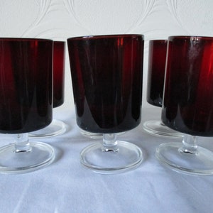 May include: Set of six red glass stemmed drinking glasses. The glasses are clear with a dark red tint and have a simple, elegant design.