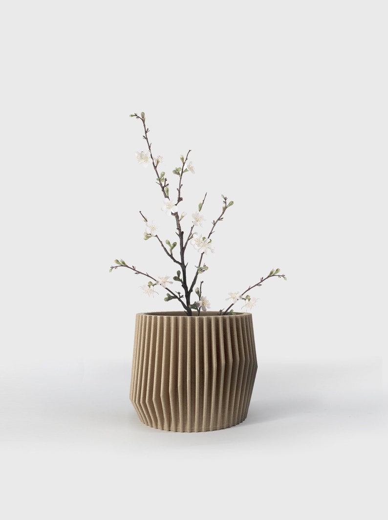 May include: A brown, ribbed ceramic planter with a small branch of white blossoms.
