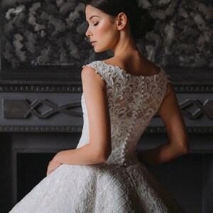 May include: A white sleeveless wedding dress with a lace bodice and a full skirt. The dress has a button-up back and is decorated with pearl-like embellishments.