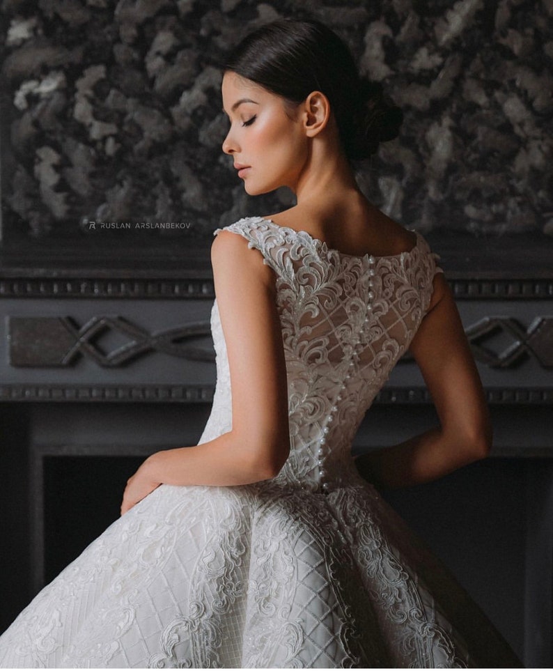 May include: A white sleeveless wedding dress with a lace bodice and a full skirt. The dress has a button-up back and is decorated with pearl-like embellishments.