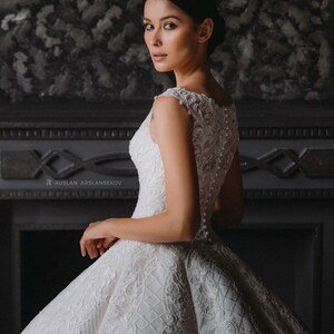 May include: A white sleeveless wedding dress with a lace bodice and a full skirt. The skirt has a quilted pattern and is adorned with intricate lace details.