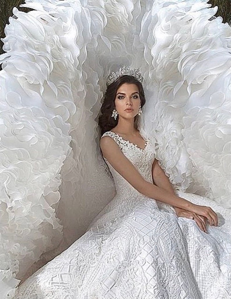 May include: A white wedding dress with a large, ruffled skirt and a lace bodice. The dress is paired with a tiara and earrings.