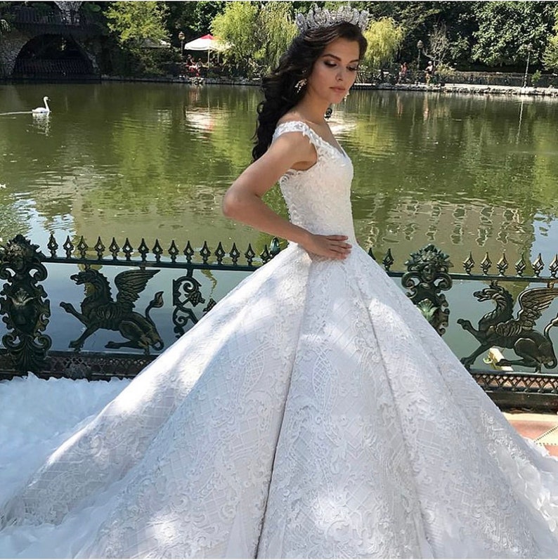 May include: A white lace wedding dress with a full skirt and a sweetheart neckline. The dress has a fitted bodice and a long train. The dress is decorated with intricate lace patterns.