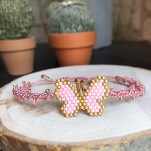May include: Pink and gold beaded butterfly charm bracelet. The bracelet is made with pink thread and features a beaded butterfly charm with gold accents.