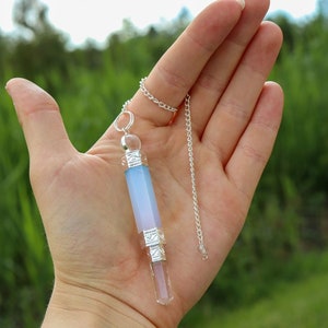 Puede incluir: Una cadena de plata con un péndulo de cristal. El péndulo es un cristal de cuarzo transparente con un cristal de ágata azul y blanco en la parte superior. El cristal mide aproximadamente 12,5 cm de largo.