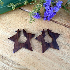 May include: A pair of wooden star-shaped earrings with a dark brown wood grain. The earrings are made of dark wood and have a simple, elegant design.