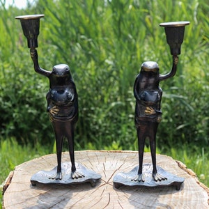 May include: A pair of bronze frog candle holders. Each frog is holding a smaller frog and has a candle holder on its head.