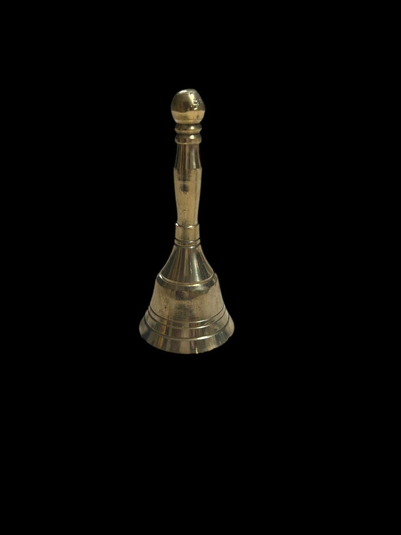 Pode incluir: Um pequeno sino dourado com o topo arredondado e a base alargada. O sino &eacute; feito de metal e tem um acabamento liso e polido.