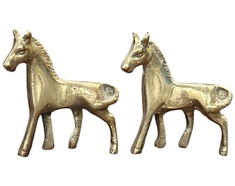 May include: Two small gold-colored metal horse figurines. The horses are standing on a white background.