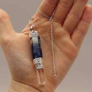 Può includere: Un pendolo di cristallo blu e bianco con una catena d'argento. Il pendolo è attaccato a una catena d'argento con un tappo decorativo in argento nella parte superiore.
