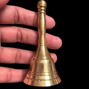 Pode incluir: Um pequeno sino dourado com o topo arredondado e a base alargada. O sino tem uma superf&iacute;cie lisa e polida e um design delicado.