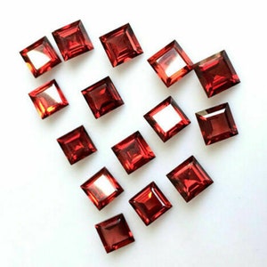 May include: A collection of 15 red square-shaped gemstones arranged in a heart shape on a white background.
