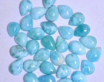 May include: A collection of 30 pear-shaped, light blue, iridescent gemstone cabochons. The cabochons are smooth and polished, with a variety of patterns and swirls.