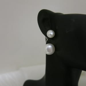 Könnte beinhalten: Ein Paar weiße Perlenohrringe mit Tropfenform. Die Ohrringe befinden sich auf einem schwarzen Präsentationsständer.