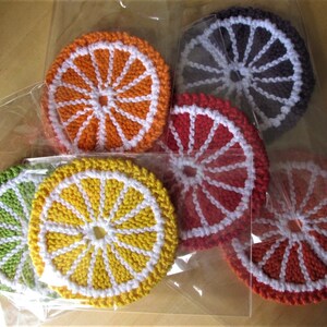 May include: Six crocheted citrus fruit coasters in various colors, including orange, yellow, green, red, and purple. Each coaster features a white crocheted center and a white crocheted rim.