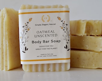 May include: A stack of four bars of oatmeal unscented body soap. The soap is a light yellow color and has a simple, elegant, natural design. The label on the front of the soap reads "Oatmeal Unscented Body Bar Soap" and includes the text "Simple, Elegant, Natural", "Good for You", "Great for the Planet", "Made in the USA", and "Net Wt. 4oz to 5oz (125g)".