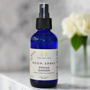 May include: A blue glass bottle with a black spray top filled with room spray. The label is white with gold lettering and reads "Simple, Elegant, Natural" and "Room Spray Spring Garden Lavender, Ylang Ylang, Frankincense" and "Made in the USA 4 oz/118ml".