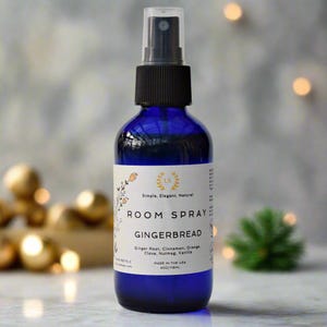 May include: A blue glass bottle with a black spray nozzle and a white label that reads "LS Simple, Elegant, Natural ROOM SPRAY GINGERBREAD Ginger Root, Cinnamon, Orange, Clove, Nutmeg, Vanilla MADE IN THE USA 4OZ/118ML".