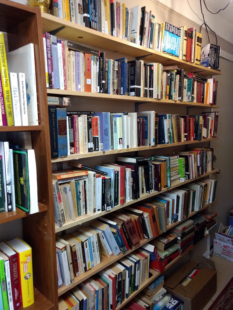 May include: A tall wooden bookshelf unit featuring multiple horizontal shelves filled with a large collection of books of varying sizes, colors, and thicknesses, arranged in vertical rows with spines facing outward for easy identification.