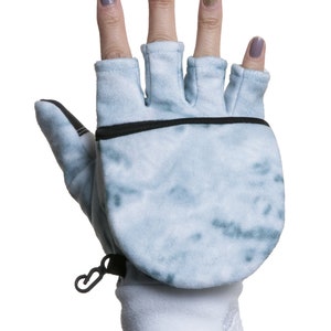 K&ouml;nnte beinhalten: Ein Paar blaue und wei&szlig;e fingerlose Handschuhe mit Fleecefutter und einer schwarzen Rei&szlig;verschlusstasche auf der R&uuml;ckseite der Hand.