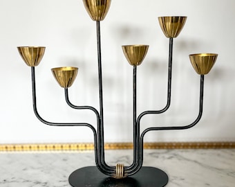 May include: A black metal candelabra with five gold candle holders. The candelabra has a modern design with curved arms and a circular base.