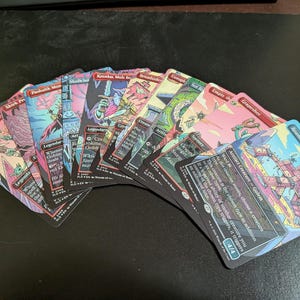 May include: A collection of fantasy trading cards with colourful illustrations and text. The cards, fanned out, display characters and creatures in shades of pink, blue, and green. Each card has a unique design and text.