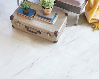 May include: A retro suitcase used as a coffee table, with books and potted plants. A grey bench with a patterned cushion and yellow blanket is behind the suitcase. The floor is white with grey veining.