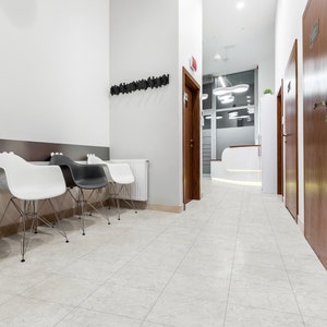 May include: A waiting area with white tiled floors, white walls, and a row of black and white chairs. There are two wooden doors in the background.