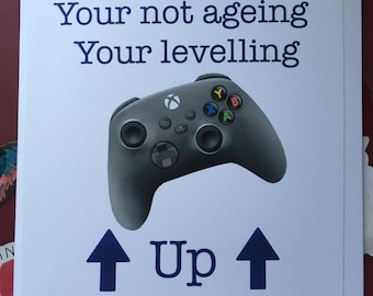 May include: A white card with blue text that reads "Your not ageing Your levelling Up" and a black and grey video game controller with coloured buttons.
