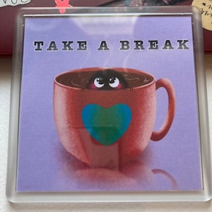 May include: A purple coaster with the text "TAKE A BREAK" in black lettering. A brown mug with a heart design and a black fuzzy creature peeking out of the mug.
