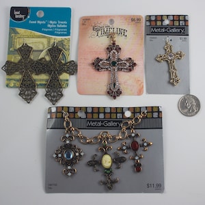 May include: Assortment of metal cross charms for jewelry making. The charms are in various styles and finishes, including gold, silver, and bronze. Some charms feature rhinestones and other embellishments. The charms are packaged on cards with prices and product information.