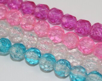 May include: Close-up of several strands of faceted beads in shades of pink, clear, and turquoise. The beads have a crackled, textured appearance, and are arranged in parallel rows against a white background. The beads are likely for jewelry making.