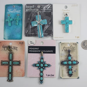 May include: Assortment of turquoise cross pendants on packaging cards. The crosses are made of metal and turquoise stones. The packaging cards have different brand names and prices.