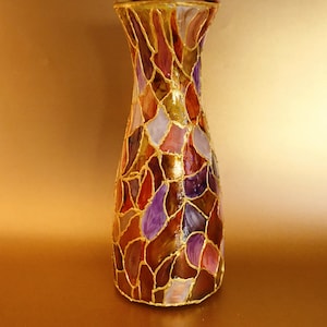 May include: A glass vase with a stained glass design. The vase is decorated with gold paint and features a variety of colours, including purple, brown, and gold.