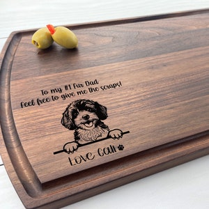 May include: A brown wooden chopping board with a personalised message that reads "To my #1 fur Dad feel free to give me the scraps! Love Call" and a black and white image of a dog peeking over the top.