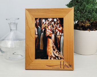 May include: A wooden picture frame with a photo of a couple surrounded by guests at their wedding. The frame has the text "EST. 2024 Howe DEX & LAURA" engraved on the bottom.