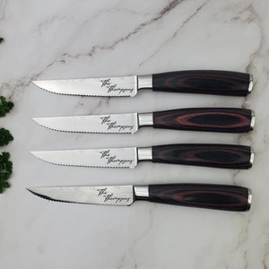 May include: Four steak knives with serrated blades and dark wood handles. The blades have a patterned design and the text "The Thompsons" is etched on each blade. The handles are a dark brown with red accents.