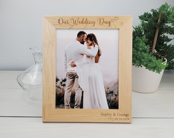 May include: A wooden picture frame with a photo of a couple embracing. The frame is engraved with the text "Our Wedding Day" and "Sophie & George 05.16.2024".