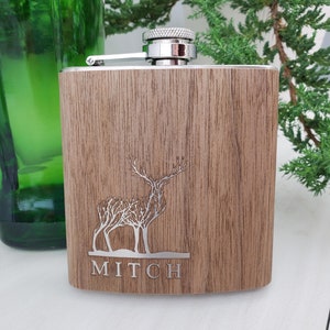 May include: A brown wooden flask with a silver top and a laser engraved design of a deer with trees for antlers. The name "MITCH" is engraved below the deer.