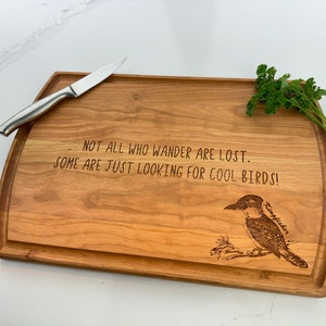 May include: A wooden chopping board with a carved design of a kingfisher and the text "NOT ALL WHO WANDER ARE LOST. SOME ARE JUST LOOKING FOR COOL BIRDS!"