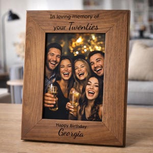 May include: A wooden photo frame with the inscription "In loving memory of... your Twenties" and "Happy Birthday Georgia". The frame contains a photograph of five people laughing and holding drinks.