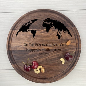 May include: A round wooden serving board with a world map design engraved on it. The board has the text "Oh the places you will go. Happy Graduation Jason. April 2022." engraved on it. The board is surrounded by a few cherries, almonds, and cashews.