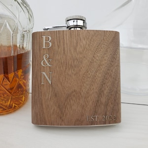 May include: A brown wooden flask with a silver top. The flask is engraved with the letters "B & N" and the text "EST. 2022".