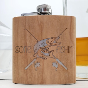 May include: A wooden flask with a silver top and a laser engraved design of a fish with crossed fishing rods and the text "gone fishin'"