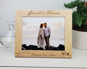 May include: A wooden picture frame with a photo of a couple standing on a beach. The frame is engraved with the names "Garrett & Simona" and the text "Happily Ever After".