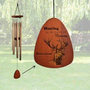 Peut inclure: Un carillon éolien avec des tubes métalliques et un capteur de vent en bois. Le capteur de vent est gravé d'une illustration de cerf et du texte : Hunting in the fields of Heaven, Peter Scott, 1963-2025. Le carillon possède un sommet en bois.