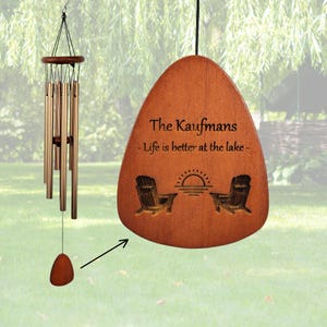 May include: A wooden wind chime with a personalized inscription that reads "The Kaufmans - Life is better at the lake -" with a sunset and two chairs engraved on the wooden piece.