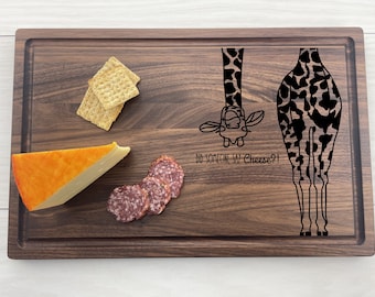 May include: A wooden cutting board with a giraffe design and the text "Did someone say Cheese?!". The board has a piece of cheese, salami, and crackers on it.