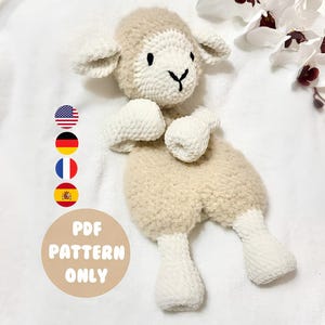 May include: A cream and white crochet lamb toy. The lamb has a fluffy body, a white face, ears, and limbs. The text "PDF PATTERN ONLY" is in a tan circle. The background is white.