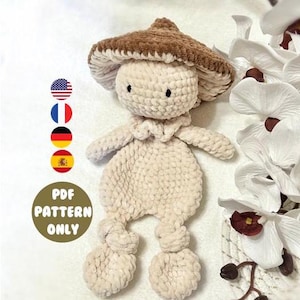 May include: A crocheted mushroom-shaped stuffed toy with a brown felt hat and a cream-coloured body. The toy is sitting on a white surface with white flowers in the background. The text "PDF PATTERN ONLY" is visible in the image.